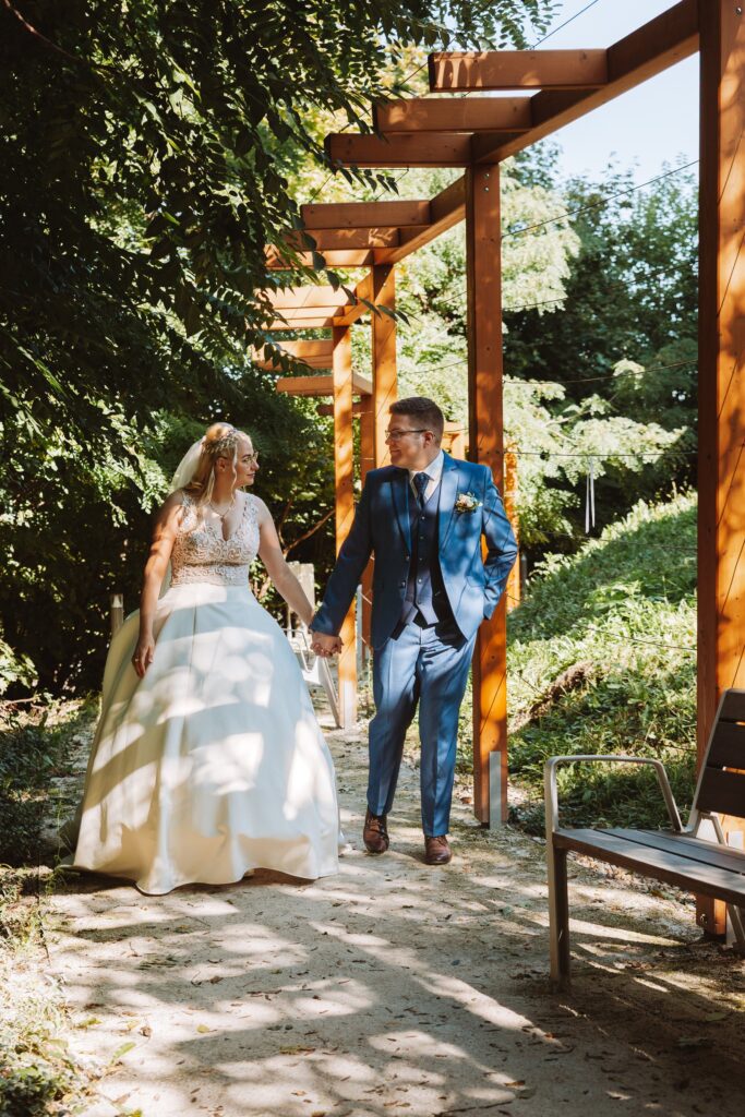 Kézen fogva sétáló pár a fa pergola alatt